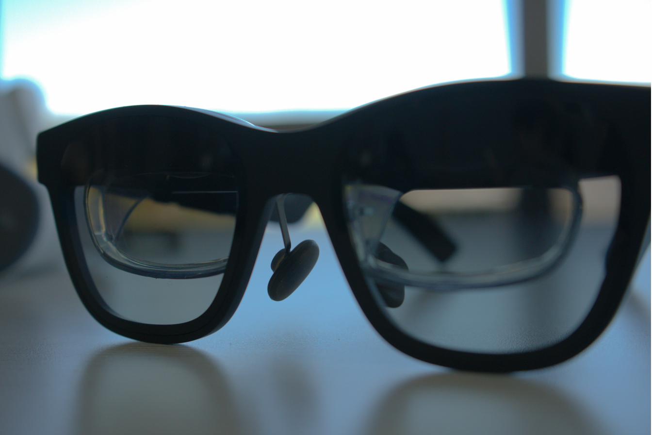 Close-up silhouette of lightweight augmented-reality smart glasses on a desk, backlit by a bright window.