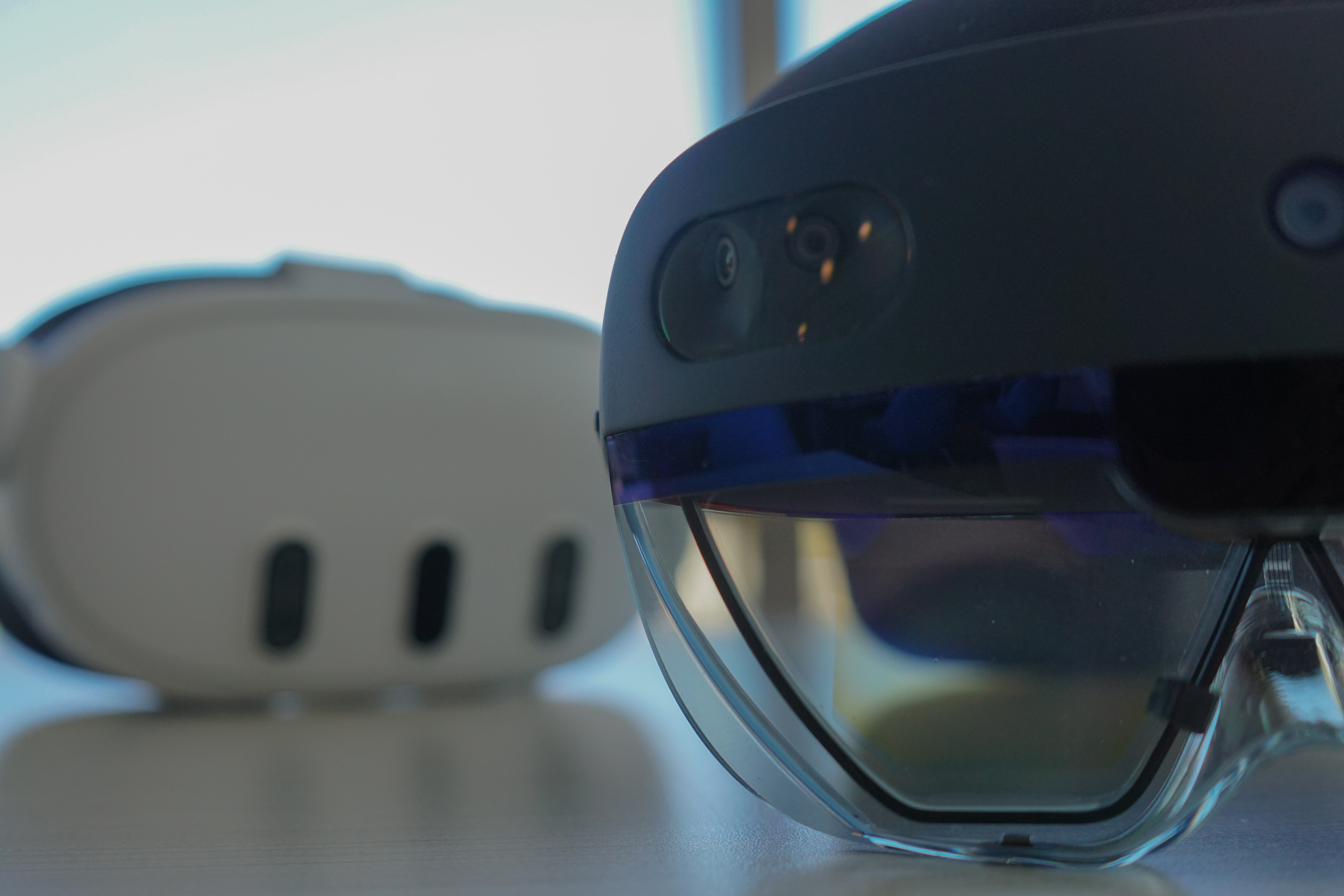Close-up of a Microsoft HoloLens 2 augmented-reality headset, with a white Meta Quest 3 in soft focus behind it.
